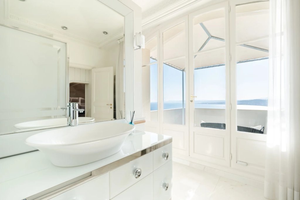 A bathroom in white, the basin before a window on the bay.