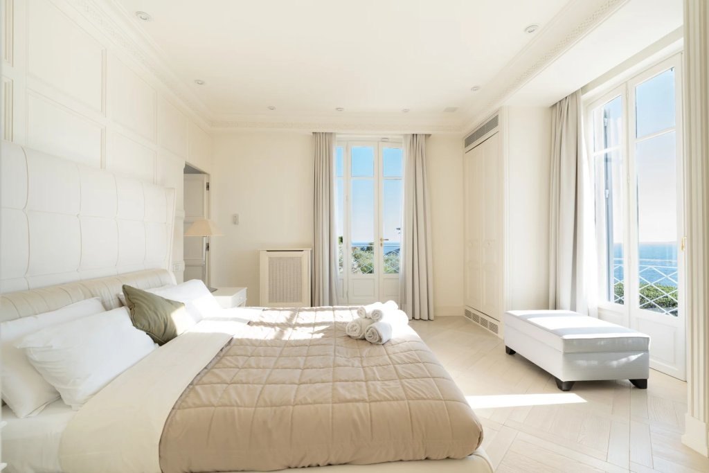 A bedroom, the sea at both windows and the bed in the morning light.