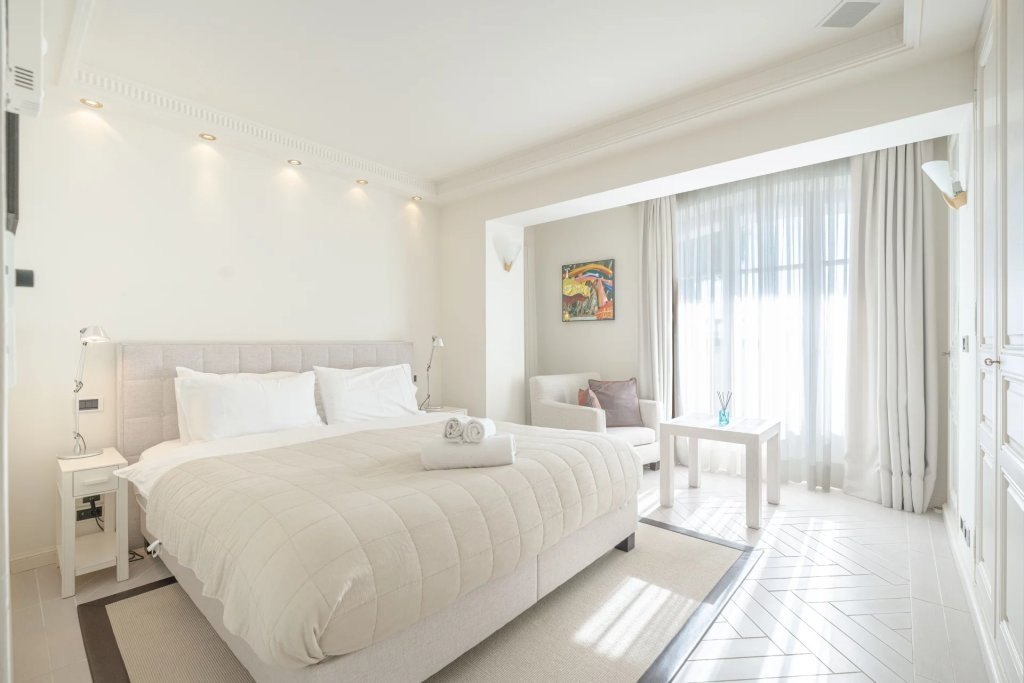 A bedroom in white, a round armchair beside the window on the sea.