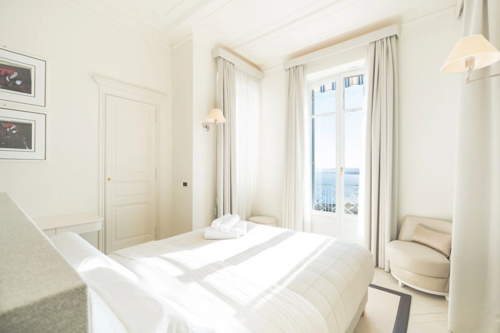 A bedroom, the bed in the light of a french window open on the sea.