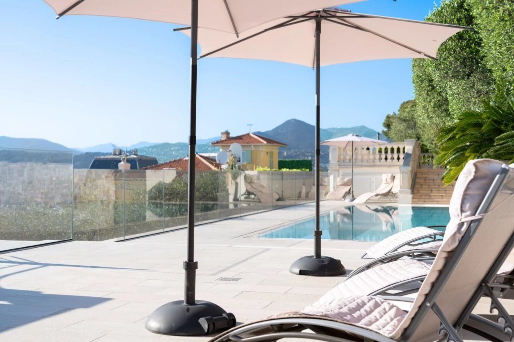 The pool and its terrace, loungers under a pale parasol, the hills of Nice behind.